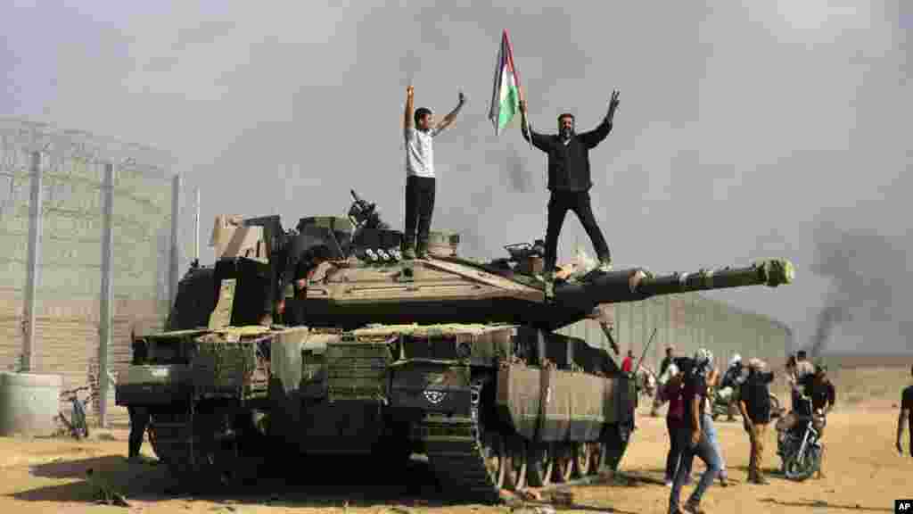 Palesztinok ünnepelnek egy megsemmisült izraeli tank mellett a Gázai övezet déli részén, a Hán Júnisztól keletre lévő kerítésnél 2023. október 7-én