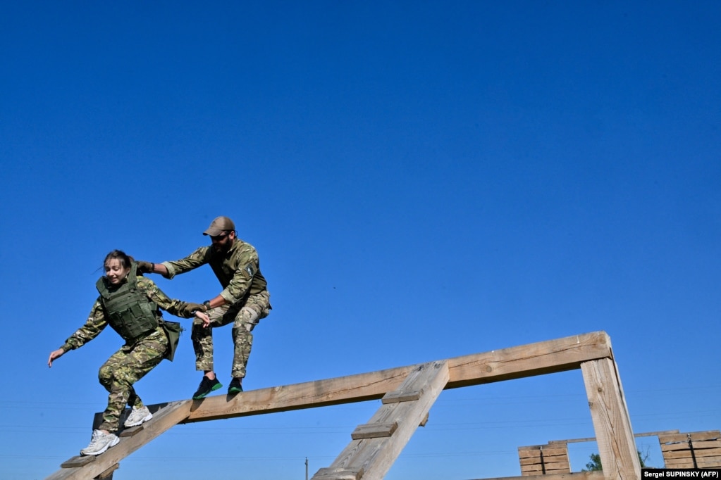 Un istruttore aiuta un cadetto che indossa la nuova uniforme militare a correre attraverso un percorso a ostacoli nel campo di addestramento fuori Kiev.