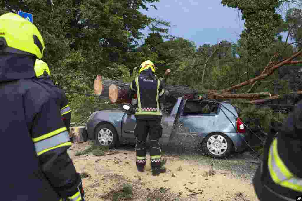 Zjarrfikësit duke e i larguar degët e pemëve nga një veturë e dëmtuar gjatë stuhisë së fuqishme në Zagreb, Kroaci. 19 korrik 2023