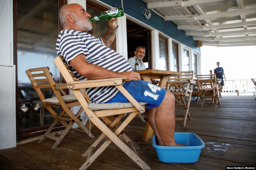 Një burrë freskon veten me një birrë ndërsa ftoh këmbët gjatë valës së parë të të nxehtit të verës më 19 qershor në Barbana, afër Ulqinit, në Mal të Zi. &nbsp;