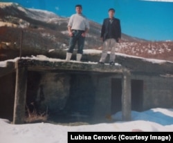 Lubisha Ceroviq (majtas) me babain e tij Lubomir Ceroviq (djathtas) duke qëndruar mbi shtëpinë e djegur në vitin 2004 në Bellopojë.