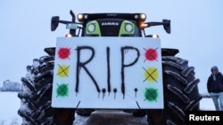Участник фермерского протеста в Германии со своим трактором, украшенным плакатом, который предрекает конец правящей коалиции