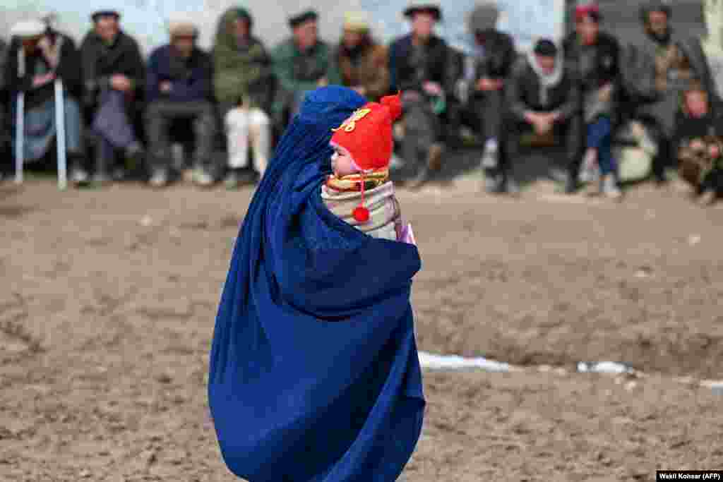 An Afghan woman in a burqa carries a child as she walks along a street in Argo district of Badakhshan Province.