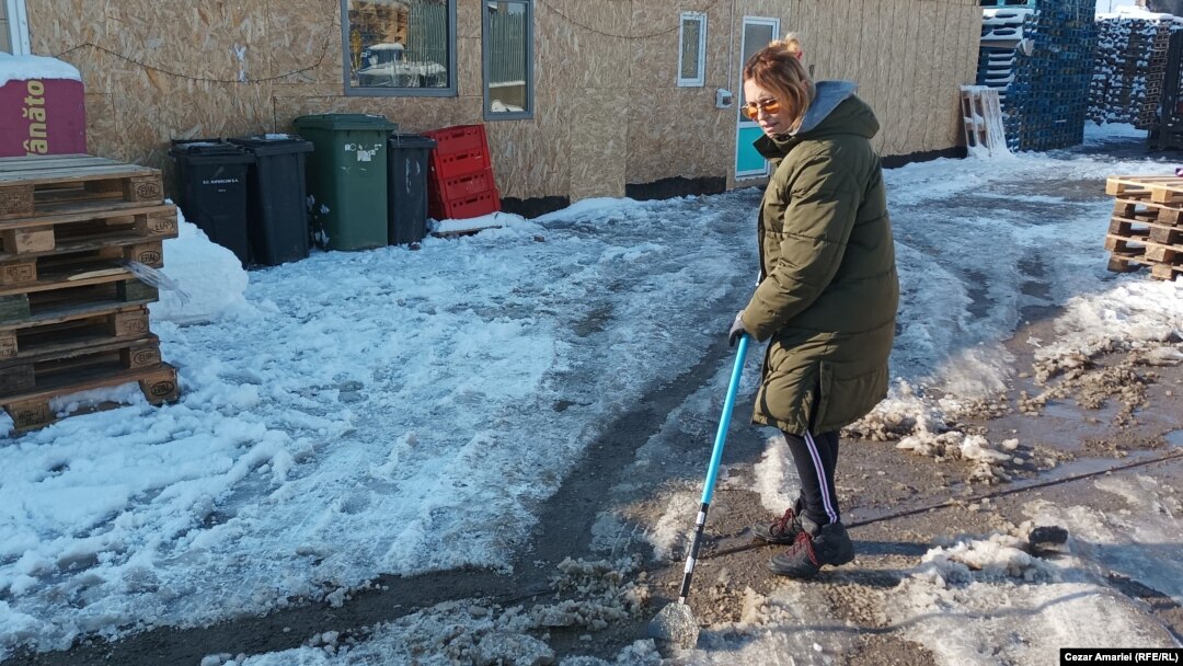 La -8 grade Celsius, sinistrata Doina Iliescu curăță curtea casei din Crevedia pentru a avea acces în containerele în care trăiesc aproape jumătate de an, de când casa lor a fost distrusă, în seara zilei de 26 august 2023.