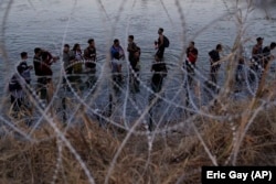 Мигранты ждут возможности перелезть через колючую проволоку, чтобы попасть из Мексики в Соединённые Штаты