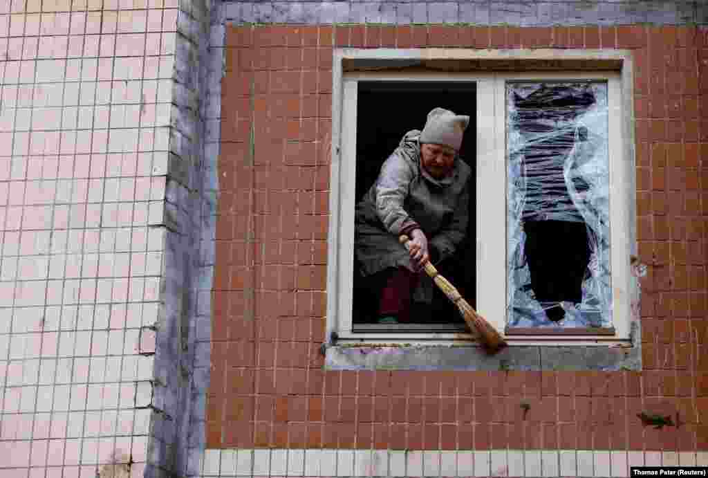 Жінка прибирає уламки знищеного вікна після російського обстрілу Києва 21 березня 2024 року &nbsp;