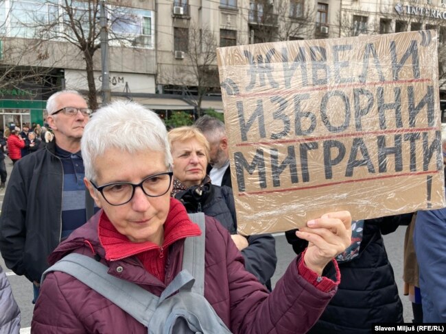 Një protestuese mban në dorë një pankartë me mbishkrimin: “Rrofshin emigrantët zgjedhorë!”