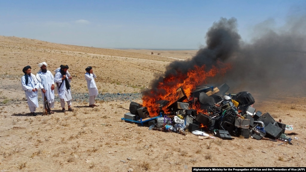 Taliban members watch the blaze after setting fire to musical instruments on the outskirts of Herat, Afghanistan, in July 2023. 