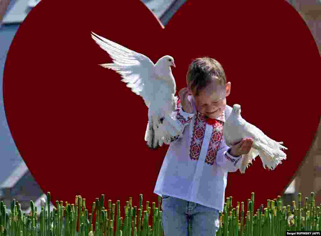 A boy wearing a &quot;vyshyvanka,&quot; a traditional Ukrainian embroidered blouse, holds pigeons as he poses for his mother on Independence Square in Kyiv during Vyshyvanka Day on May 18.