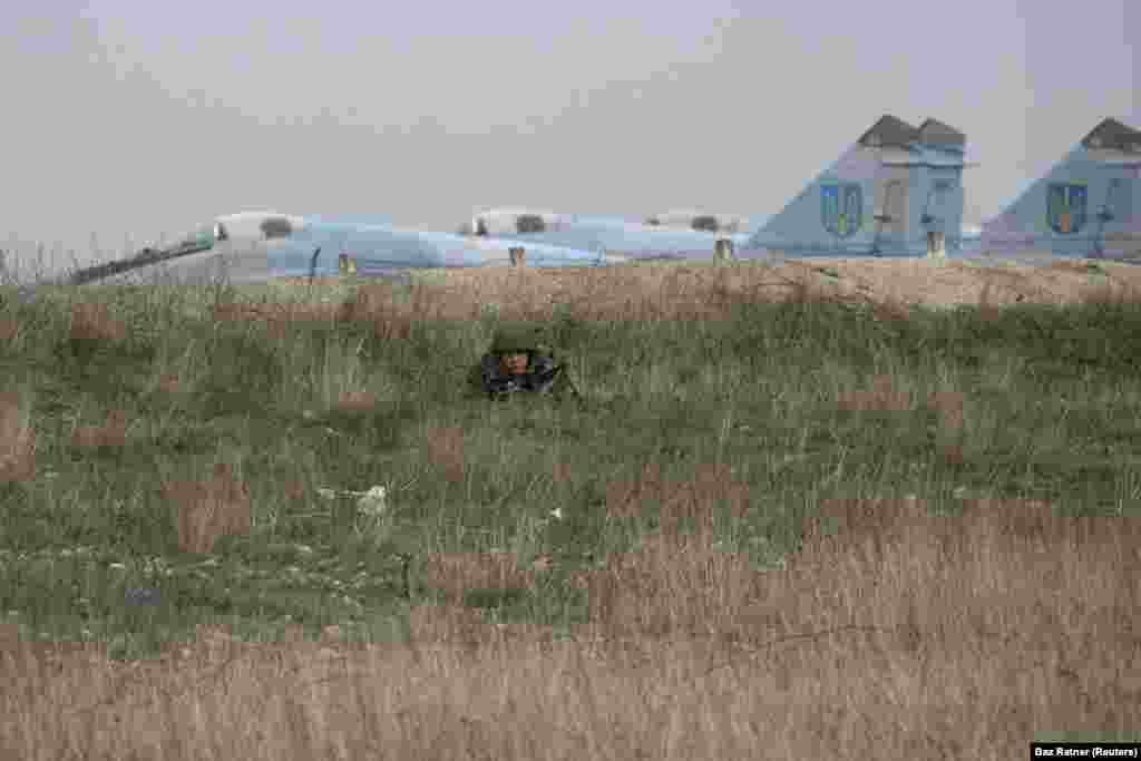 A Russian soldier watching Ukrainian military personnel at the Belbek airport, near Sevastopol. The Ukrainian Air Force base became one of the last Ukrainian holdouts in Crimea as its commander refused to hand over the site to Russian troops. He was eventually detained by Russian forces and Ukrainian personnel were forced out.&nbsp;