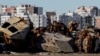 Цивільні автомобілі й військова техніка, знищені під час нападу Росії на Україну, перед житловими будинками в місті Буча, 30 березня 2023 року