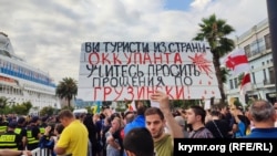 Протестующий держит плакат с обращением к туристам из страны-оккупанта