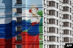 Një ndërtesë banimi e porsandërtuar në Mariupol shfaq fotografinë e një vajze të veshur me një fustan me ngjyra të flamurit rus, gusht 2023.
