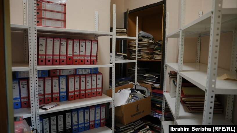 Një zyrë e vogël ku ruhen disa libra me të dhënat e pacientëve dhe disa folderë me shënime.