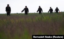 Membrii Serviciului de Stat de Urgență al Ucrainei inspectează o zonă pentru mine și obuze neexplodate în apropierea satului Blahodatne, din regiunea NIkolaev, pe 10 mai.