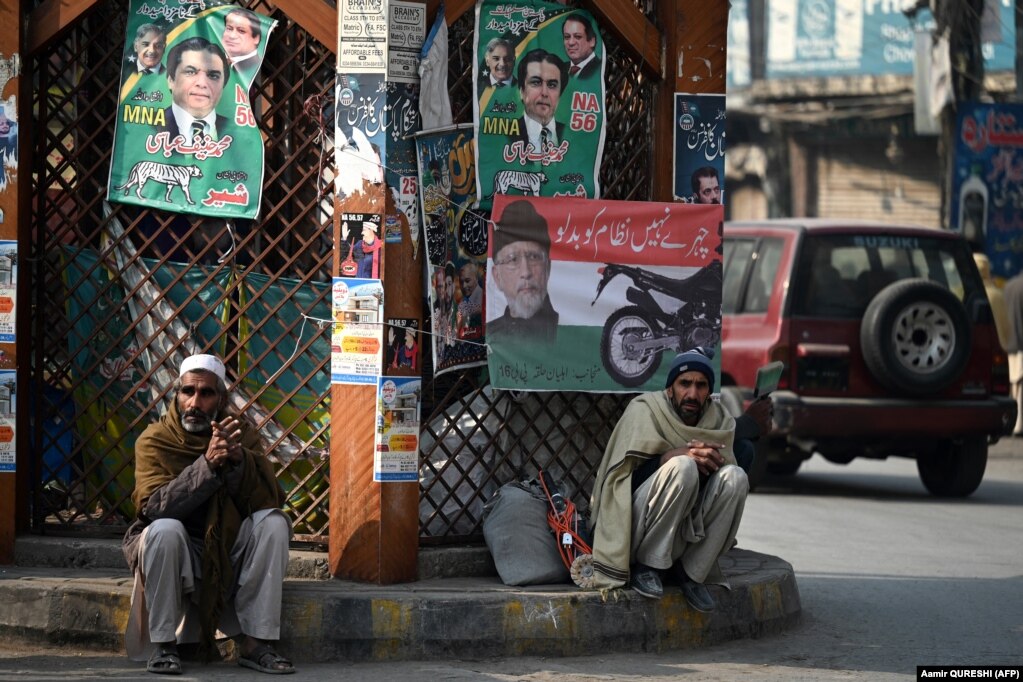 Punëtorë të ulur pranë një gardhi rrethojash ku janë ngjitur posterë si pjesë e fushatës zgjedhore në një rrugë në Ravalpindi. Lista përfundimtare e kandidatëve do të publikohet nga Komisioni Zgjedhor i Pakistanit më 23 janar. &nbsp;