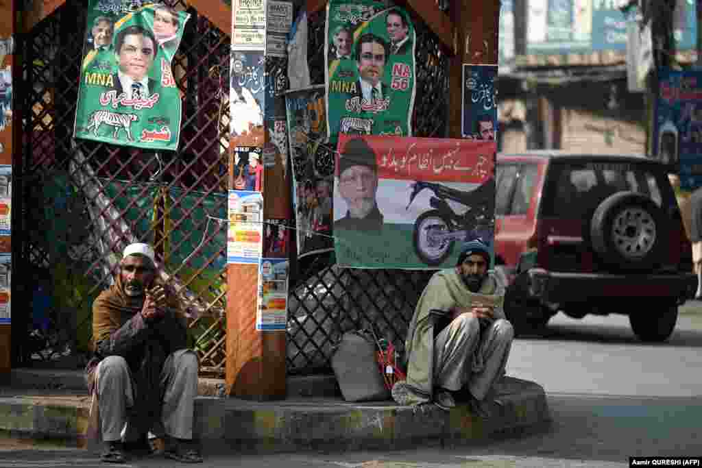 Laborers sit next to election campaign posters on a roadside in Rawalpindi. The final list of candidates is set to be issued by the Election Commission of Pakistan on January 23. &nbsp;