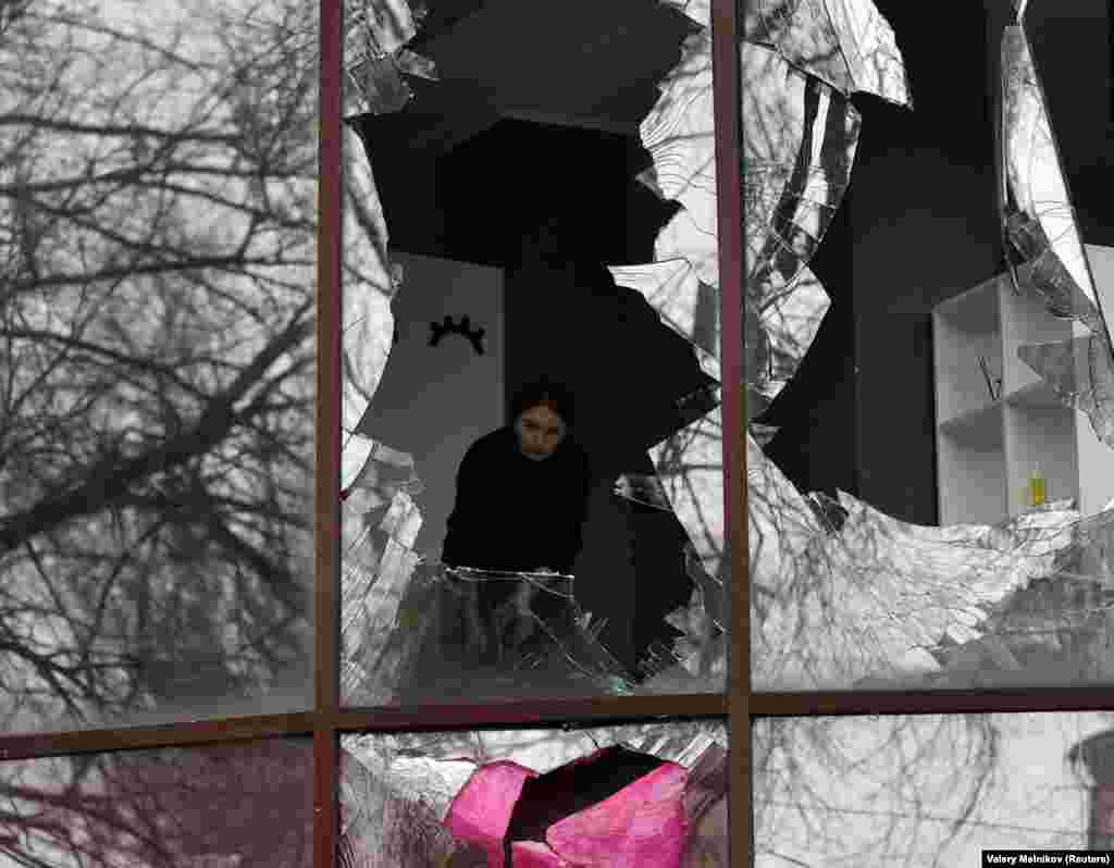 A woman removes shards of glass from broken windows in a building housing a beauty salon following recent shelling in the course of the Russia-Ukraine war in Donetsk, in Russian-controlled Ukraine.