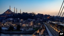 Xhamia Sulejman shihet lart, ndërsa poshtë shihen këmbësorët teksa ecin përgjatë urës së metrosë, Halic, Stamboll, 10 mars 2024.