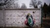 Ukraine -- A wreath is photographed leaning against a shrapnel-damaged wall in the cemetery where the funeral for Kasich, 42, is being held, in Bucha, near Kyiv, Ukraine, Friday, Feb. 17, 2023. 