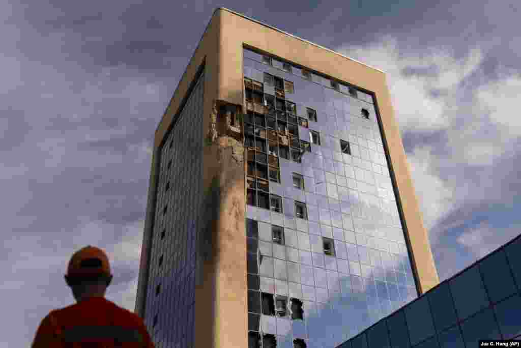 A maintenance worker stands outside a damaged government building in Kyiv following Russian drone attacks.