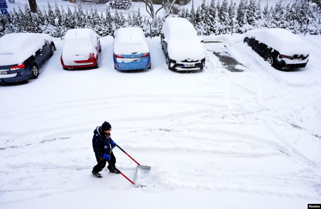 Një burrë me një lopatë dore duke larguar borën nga hapësirat e parkingut pranë një ndërtese banimi në Stokholm, Suedi, 4 janar 2024.