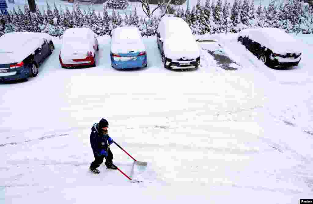 Një burrë me një lopatë dore duke larguar borën nga hapësirat e parkingut pranë një ndërtese banimi në Stokholm, Suedi, 4 janar 2024.