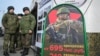 Soldații ruși stau lângă un centru mobil de recrutare cu un panou care conține informații despre plăți în Rostov-pe-Don, Rusia.