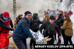 Українські рятувальники несуть поранену жінку на місці ракетного обстрілу житлового будинку в Харкові, на північному сході України, 23 січня 2024 року