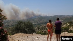 Švicarski turisti promatraju šumski požar koji gori u blizini sela Archangelos, otok Rodos, Grčka, 24. juli