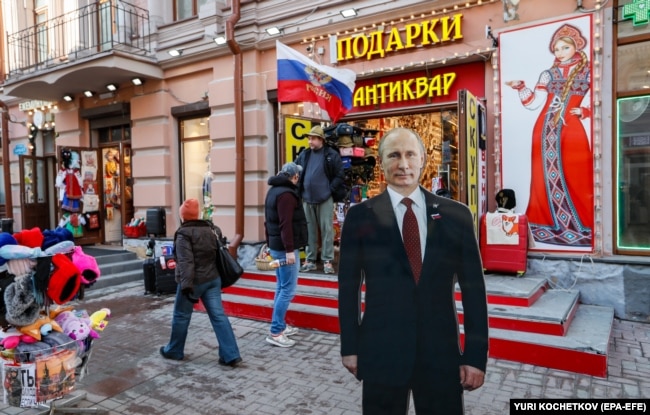 People walk past a cardboard cutout of Putin on a street in Moscow on March 13. “There is no way you can call this an election. And the majority of the population understands this perfectly,” one analyst said of Russia’s March 15-17 presidential vote.