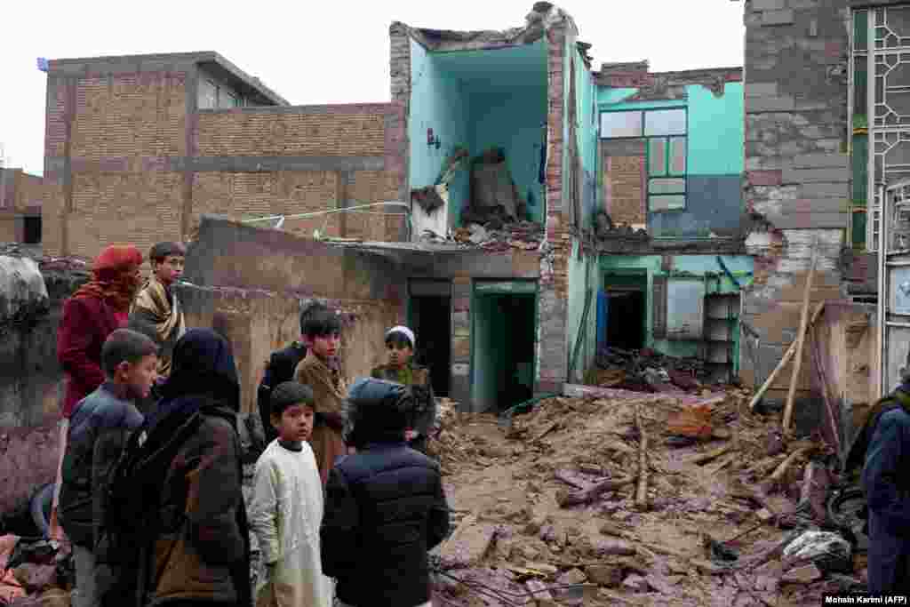 Onlookers gather at a collapsed house where flooding claimed the lives of five family members and injured two others. A local imam said the house had been weakened by the devastating earthquake that struck Herat in October.