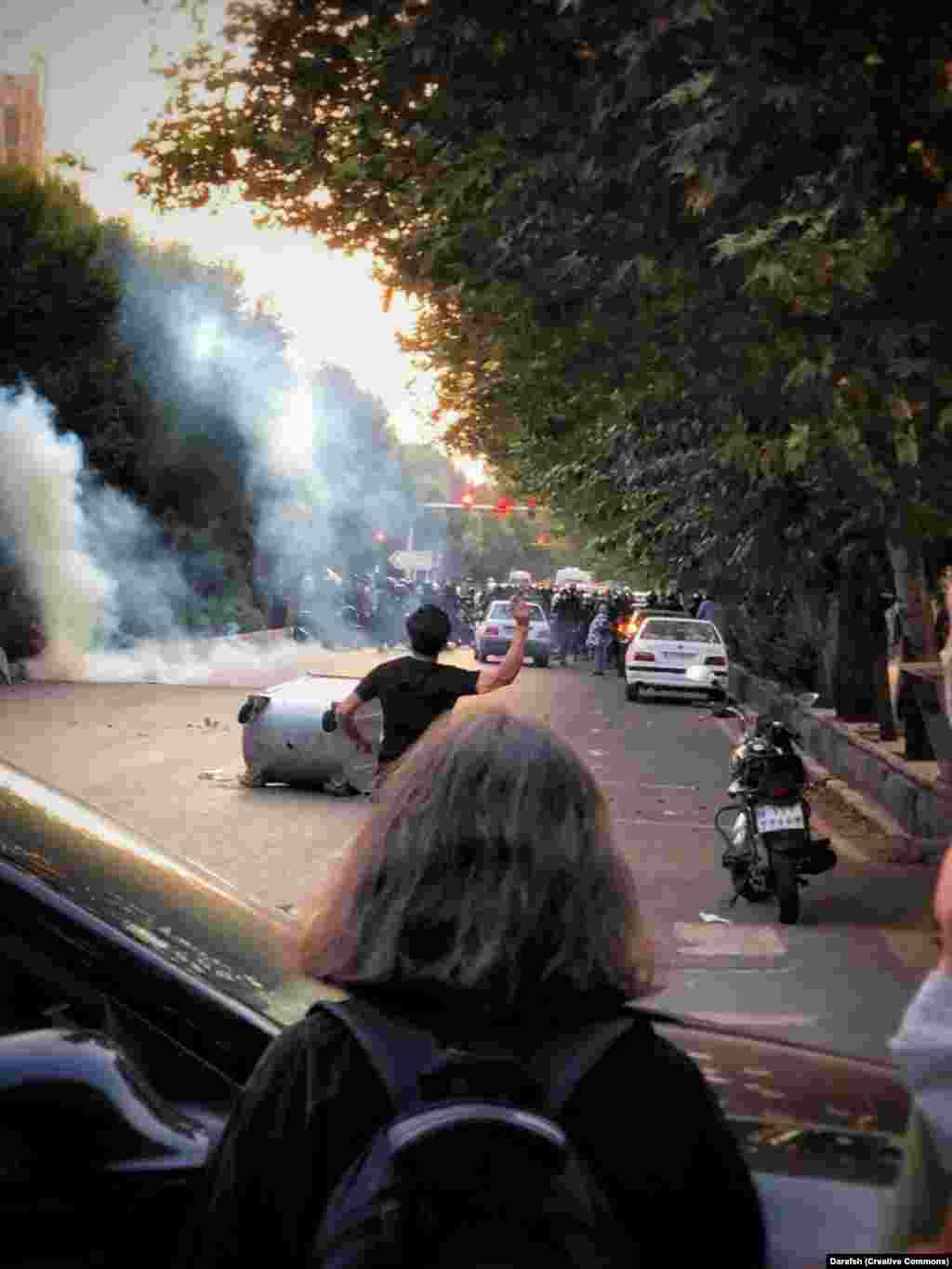 A September 2022 photo shows a young woman watching violent protests in Tehran following the death of Mahsa Amini. Throughout the widespread unrest that followed the September 2022 death of Amini while in the custody of the morality police, increasing numbers of women opted not to wear their hijabs. The head scarves have been mandatory in Iran since shortly after the 1979 Islamic Revolution. &nbsp;