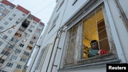 Жінка прибирає розбите скло в своїй квартирі поблизу пошкодженого багатоповерхового житлового будинку після повідомлення про атаку безпілотника у Воронежі, Росія, 16 січня 2024 року