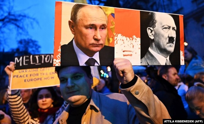 Плакат із зображенням російського президента Володимира Путіна й Адольфа Гітлера на акції біля посольства РФ в Угорщині у другі роковини масштабного вторгнення Росії до України. Будапешт, 24 лютого 2024 року