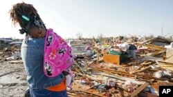 Një grua me një fëmijë në krah shikon shtëpinë e saj të shkatërruar nga tornadoja në Rolling Fork të Misisipit. 25 mars 2023.
