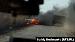 Українські військові проїжджають повз машину, яка горить, біля міста Авдіївка, листопад 2023 року