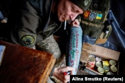 Fotografie de arhivă - un militar ucrainean scrie pe un proiectil numele camarazilor căzuți în luptă.