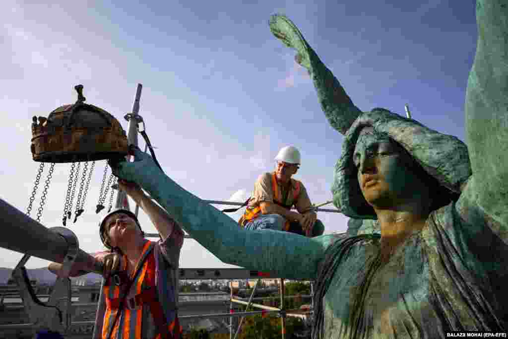 An restorer standing on scaffolding examines the considerably eroded statue of Archangel Gabriel, the centerpiece of Heroes Square in Budapest.