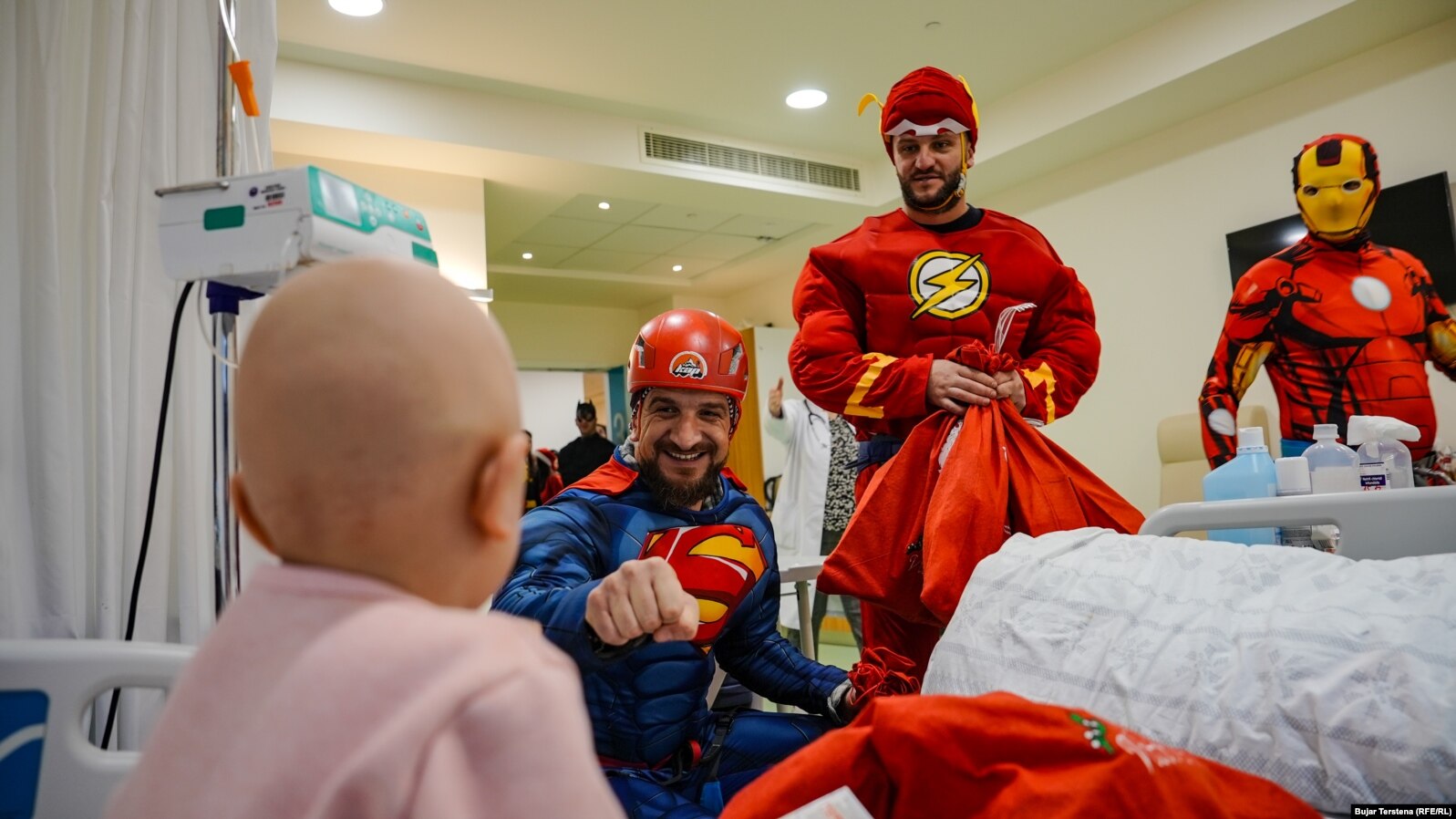 Berat Rexhepaj, i veshur në kostumin e Superman, viziton një fëmijë në repartin e Onkologjisë pediatrike në QKUK bashkë me vullnetarë të tjerë.