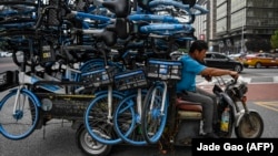Мужчина едет на трехколесном велосипеде, нагруженном велосипедами, по улице в Пекине, 11 августа 2023 года
