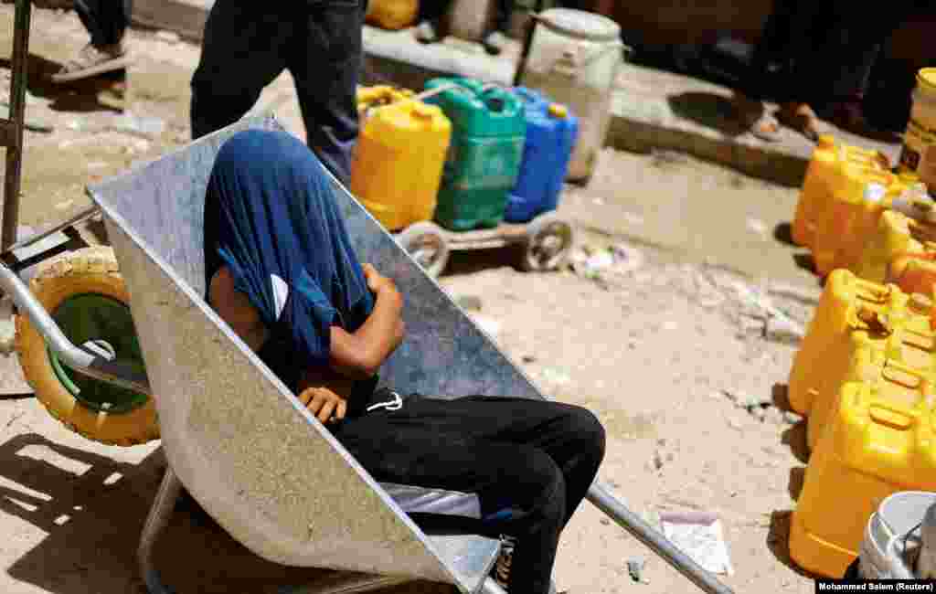 Një djalë palestinez mbulohet që të mbrohet nga dielli duke përdorur bluzën e tij, ndërsa pret të mbushë ujë në Han Junis, maj 2024.&nbsp;
