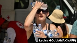 Egy nő hideg palackos vízzel hűti magát a görög Vöröskereszt jóvoltából az athéni Akropolisz bejáratánál 2023. július 20-án.