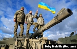 Ukrainian soldiers hold a Ukrainian flag as they pose on top of a Challenger 2 tank during training at Bovington Camp, near Wool in southwestern England, on February 22.