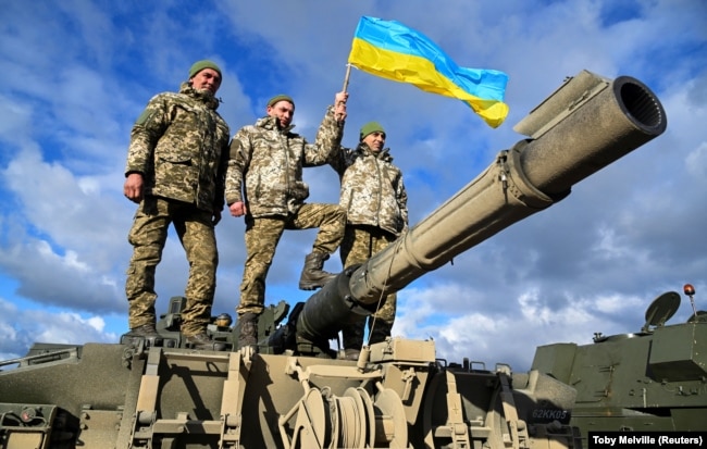 Ukrainian soldiers hold a Ukrainian flag as they pose on top of a Challenger 2 tank during training at Bovington Camp, near Wool in southwestern England, on February 22.