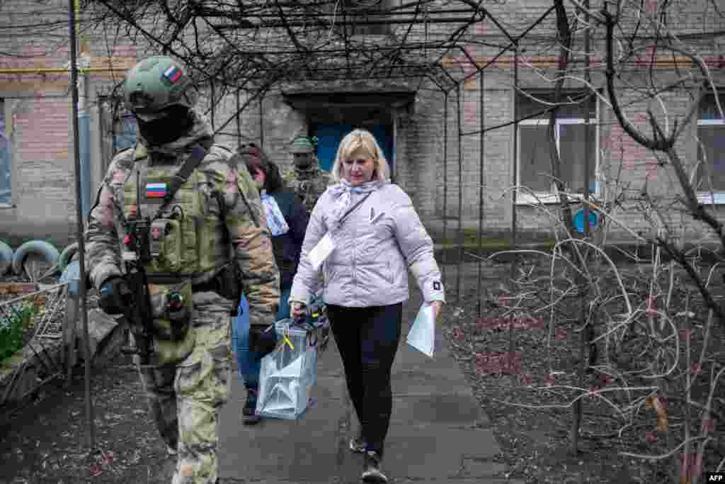 Članovi lokalne izborne komisije u pratnji vojnika obilaze glasače u okupiranom ukrajinskom regionu Donjeck, gde je omogućeno rano glasanje, 14. mart 2024. Ukrajinska i zapadne vlade osudile su Rusiju zbog održavanja glasanja u okupiranim ukrajinskim regionima, nazivajući ih nezakonitima.