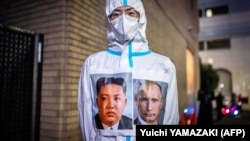 Чоловік у захисному костюмі з портретами лідера Північної Кореї Кім Чен Ина та президента Росії Володимира Путіна під час святкування Гелловіну. Токіо, Японія, 30 жовтня 2022 року 