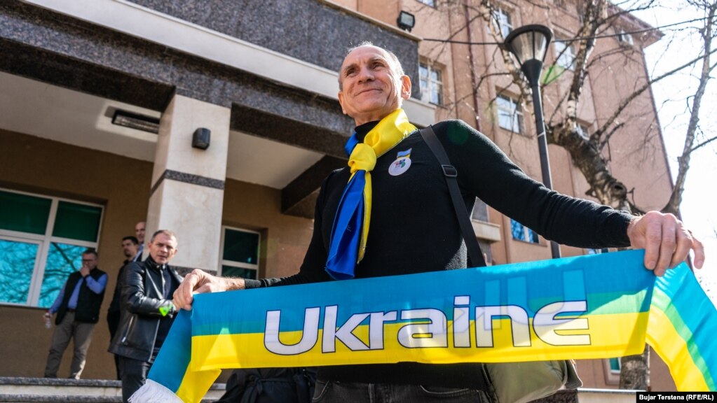 Gaztari ukrainas i strehuar në Kosovë, Serhii Shevchenko, duke buzëqeshur, teksa në duar mban një shall me mbishkrimin &quot;Ukraina&quot;, më 24 shkurt.