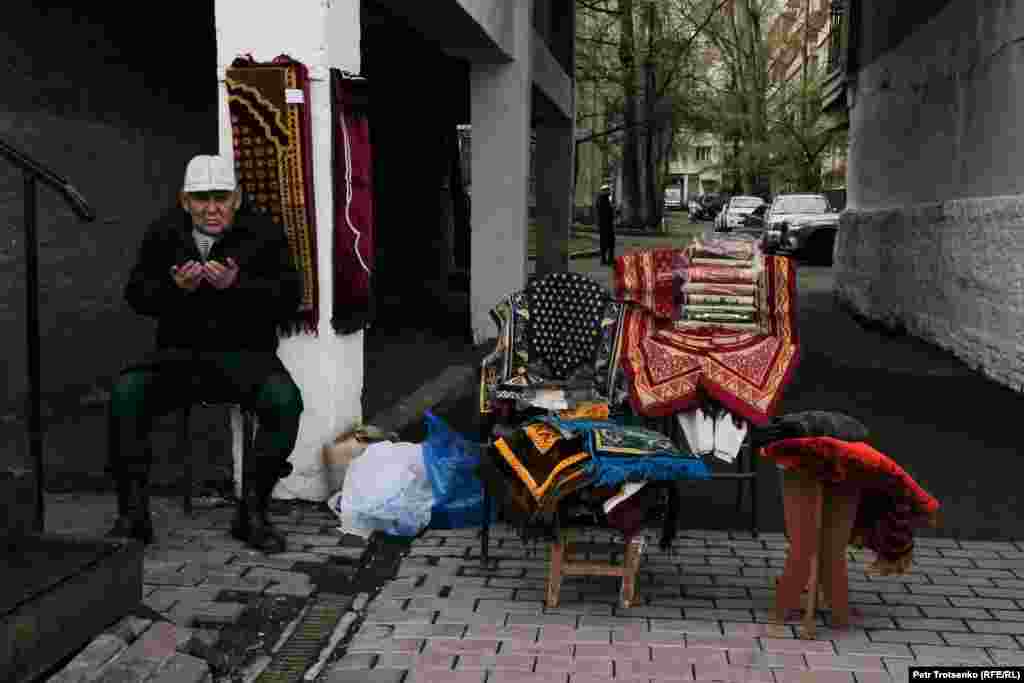 Торговец ковриками для молитвы и другой мусульманской атрибутикой молится у своего товара