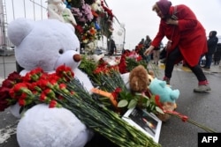 Женщина возлагает цветы к импровизированному мемориалу перед зданием «Крокус Сити Холл» на следующий день после теракта в Красногорске под Москвой, 23 марта 2024 года